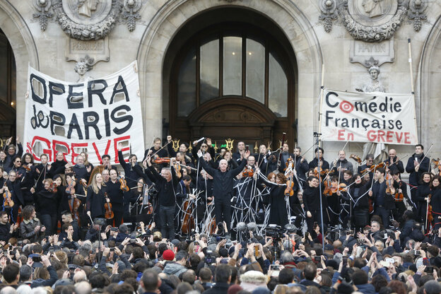 Vor dem Eingang der Oper hängen Transparente, ein Orchester spieltvor einer Menschenmenge