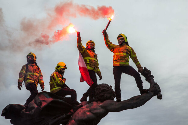 vier Feuerwehrleute mit Pyrotechnik sitzen auf einer Statue.