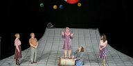Fünf Menschen auf einer Bühne, die wie eine Matratze aussieht. eine Frau steh auf einer Tonne