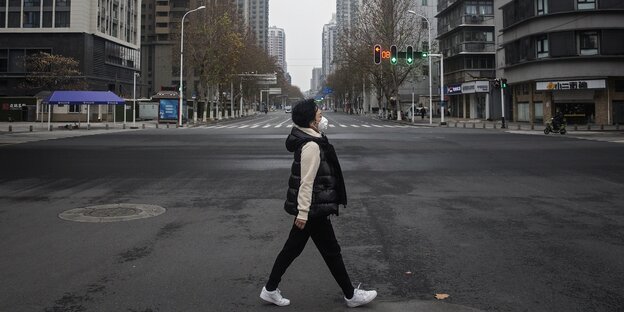 Ein Frau mit Mundschutz überquert über eine leere Straße.