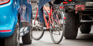 Ein Fahrrad fahrende Person zwängt sich zwischen zwei Autos hindurch