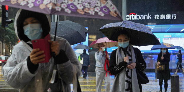 Menschen mit Atemschutzmasken und Schirm laufen durch den Regen
