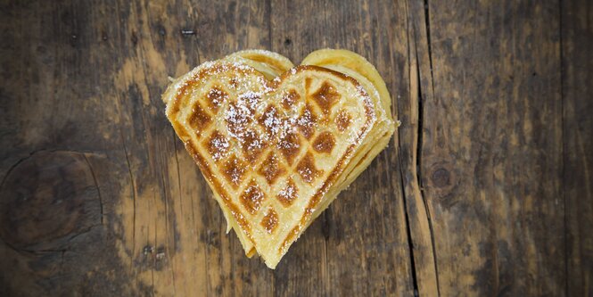 Eine Herzwaffel mit ein wenig Puderzucker liegt auf einer Holzoberfläche