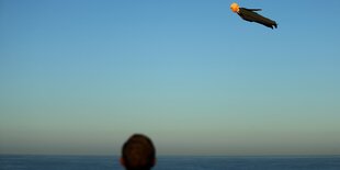 blauer Himmel, an dem eine Trumpfigur fliegt. Ein Mann schaut zu der fliegenden Figur hoch