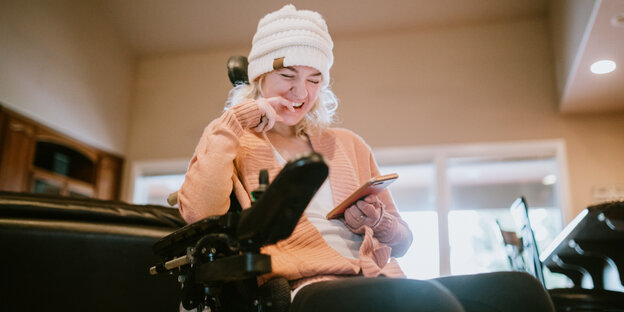 Eine Frau, die im Rollstuhl sitzt und auf ihr Smartphone blickt