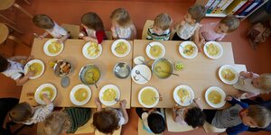 Kinder sitzen um einen Tisch mit Suppentellern