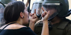 Eine Demonstrantin zeigt einem behelmten Polizisten die Mittelfinger