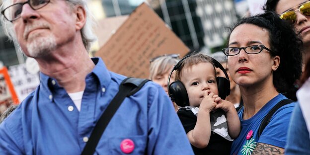 DemonstrantInnen mit Pappschildern und und einem Kind mit Ohrschützern.