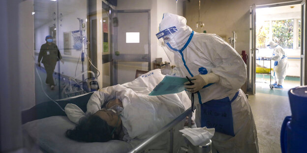Ein Mann im Schutzanzug beugt sich über eine Patientin in einem Krankenbett.