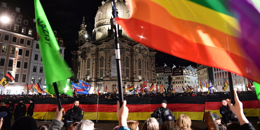 Pegidisten vor der Frauenkirche, im Vordergrund Gegendemonstrierende, die Regenbogenfahnen schnwenken