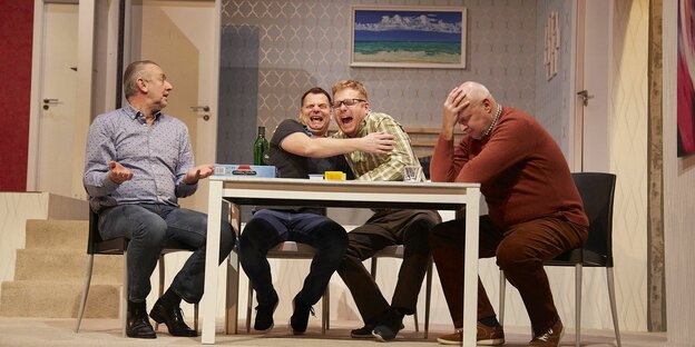 Szene aus einem Boulevardtheaterstück, in der vier Männer um einen Tisch sitzen