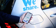 Ein Smartphone mit einer Carsharing App wird vor ein Fahrzeug gehalten.