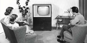 In einer Schwarzweißaufnahme sitzt eine Familie vor einem Fernseher.
