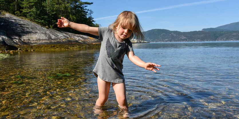 Ein Kind steht mit dem Füßen an einer felsigen Küste im Wasser.