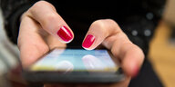 Nahaufnahme der Hände einer Frau mit roten Fingernägeln, die auf einem Smartphone tippt