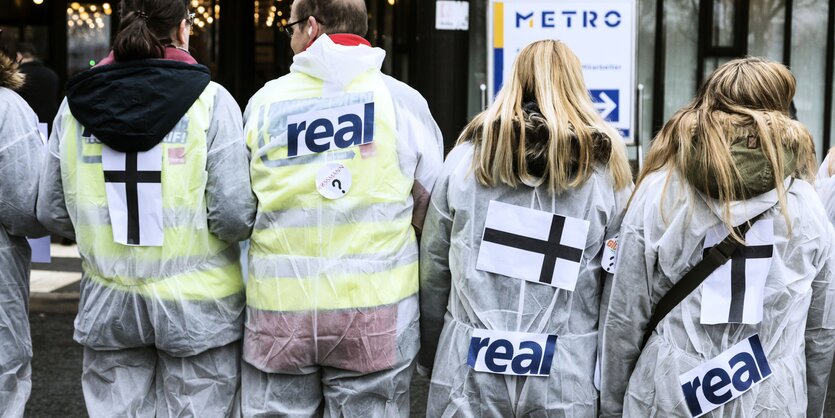 Demonstranten gegen den Verkauf der Supermarktkette Real zeigen der Kamera den Rücken.