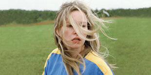 Nahaufnahme einer jungen Frau auf einer Wiese, der Wind weht ihr die Haare ins Gesicht