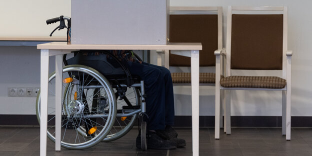 Ein Mensch im Rollstuhl gibt in einem Wahllokal seine Stimme ab.