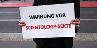 Ein mann hält ein Schild mit der Aufschrift Warnung vor Scientology