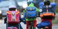 Drei Kinder mit Schulränzen auf Fahrrädern von hinten