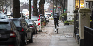 Radfahrer auf engem Geh- und Radweg, links Bäume und Autos