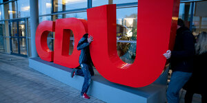 Das CDU-Logo in großen roten Lettern, zwei Menschen ziehen und schieben rechts an dessen "U" herum