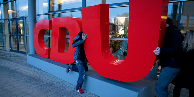 Das CDU-Logo in großen roten Lettern, zwei Menschen ziehen und schieben rechts an dessen "U" herum