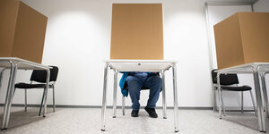 Ein Wahllokal. Menschen sitzen in sichtgeschützten Wahlkabinen und geben ihre Stimmen ab.