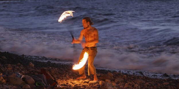 Mann mit Feuertöpfen nachts am Strand
