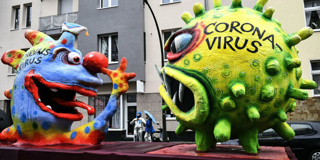 Ein Karnevalwagen mit einem grünen Coronavirus und einem Narrenkopf