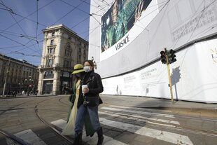 Zwei Frauen tragen einen Mundschutz und überqueren eine Straße.