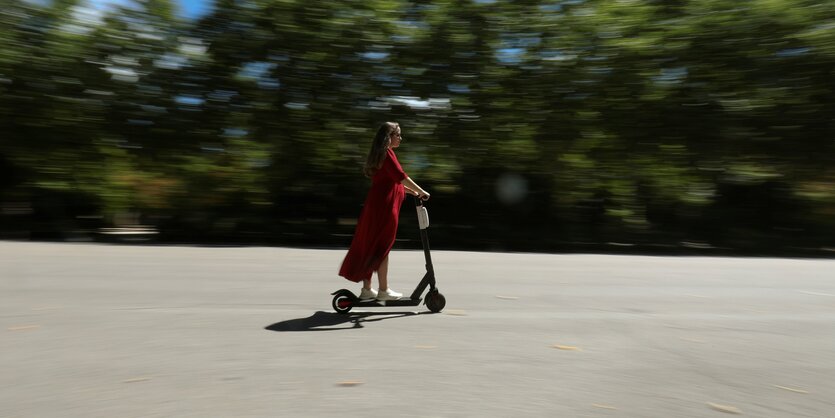 Frau auf einem Roller vor Bäumen