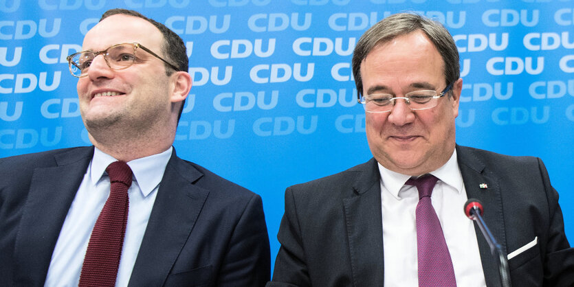 Jens Spahn und Armin Laschet sitzen hinter einem CDU-Logo und lächeln