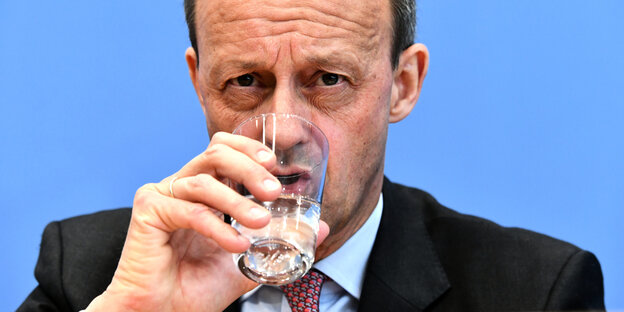 Friedrich Merz trinkt bei einer Pressekonferenz ein Glas Wasser.