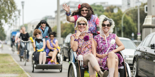 Als Putzfrau verkleidetete Frauen lassen sich mit einem Radtaxi chauffieren