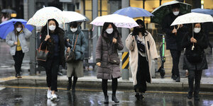 Frauen mit Gesichtsmasken und Regenschirmen auf der Straße