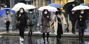 Frauen mit Gesichtsmasken und Regenschirmen auf der Straße