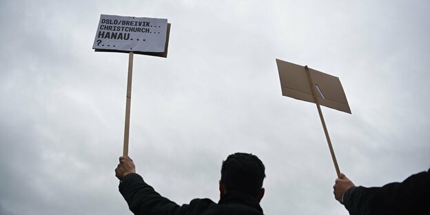 Zwei Teilnehmer eines Trauermarsches in Hanau recken Plakate in die Luft.