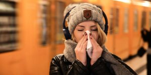 Eine junge Frau mit Kopfhörer niest in ein Taschentuch