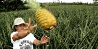 Eine Farmerin steht in einem Ananasfeld und wirft eine Ananas