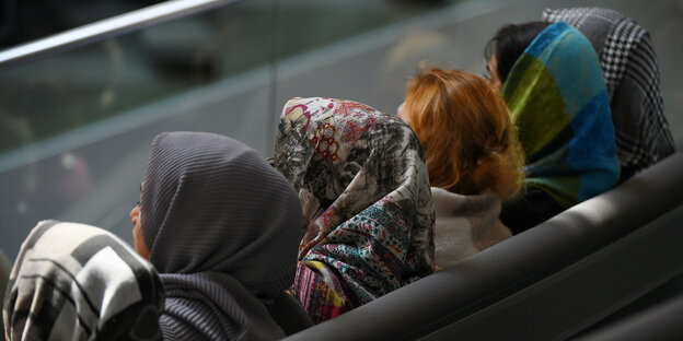 Frauen mit Kopftüchern sitzen nebeneinander, mit dem Rücken zum Betrachter
