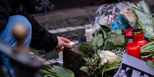 Ein Mann legt auf der Straße eine Kerze neben Blumesträuße