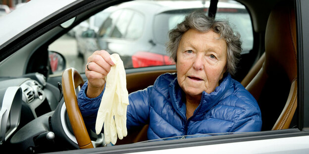 Ein eFrau zeigt ihre Schutzhandschuhe aus dem Autofenster.