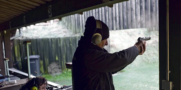 Zwei Männer mit Ohrenschützern schießen mit Waffen auf ein Ziel