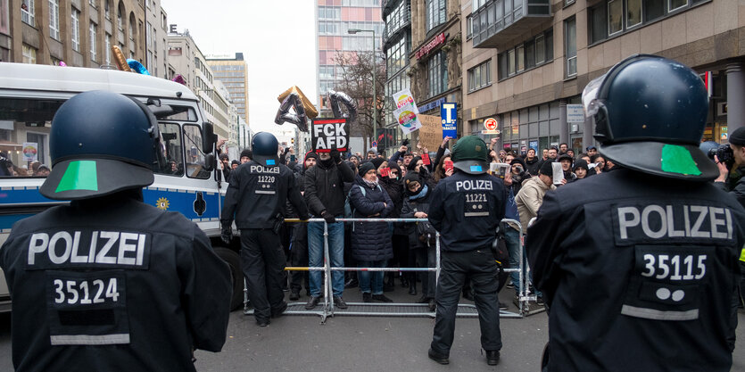 Demonstranten hinter Polizisten und Absperrgittern