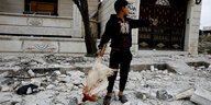 Ein Junge mit einem toten Huhn in der Hand steht auf einer mit Schutt übersäten Straße
