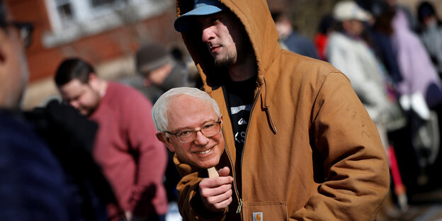 Ein Mann hält eine Bernie-Sanders-Maske in der Hand