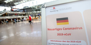 In einem Terminal des Hamburger Flughafens steht eine Infotafel, die auf das Risiko durch das Corona-Virus hinweist