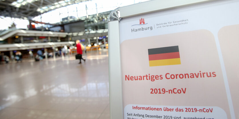 In einem Terminal des Hamburger Flughafens steht eine Infotafel, die auf das Risiko durch das Corona-Virus hinweist