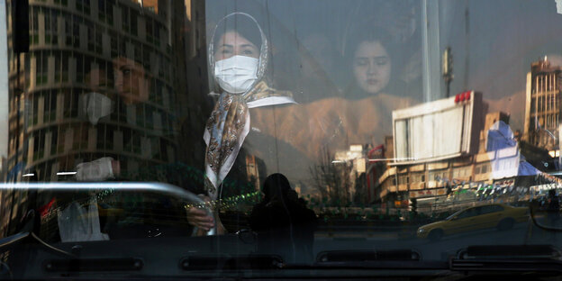 Frau mit Mundschutz hinter einer spiegelnden Busscheibe